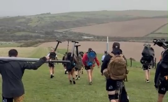 Men carrying gym equipment while cross-country walking.