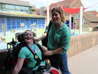A young girl in a wheelchair who is next to her mum standing.