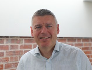Man headshot smiling at the camera with a shirt on.
