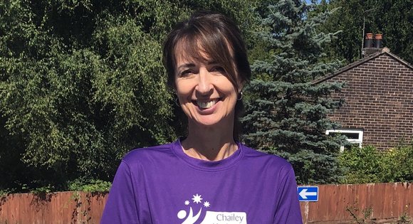 Paula standing up outside and smiling, wearing a purple t-shirt