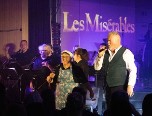 Men singing on a stage with purple lighting.