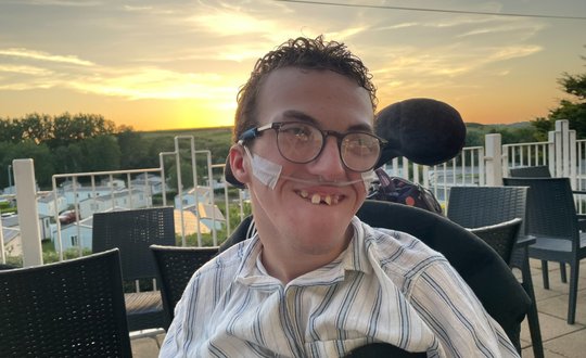 Boy smiling outside with a sunset behind him.