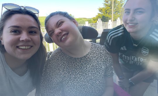 Girl outside smiling with two support workers..
